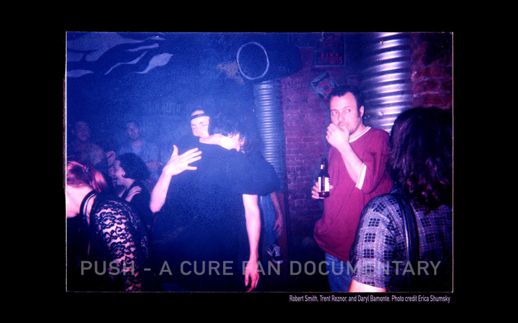Robert Smith and Trent Reznore hug at a nightclub in a small crowd